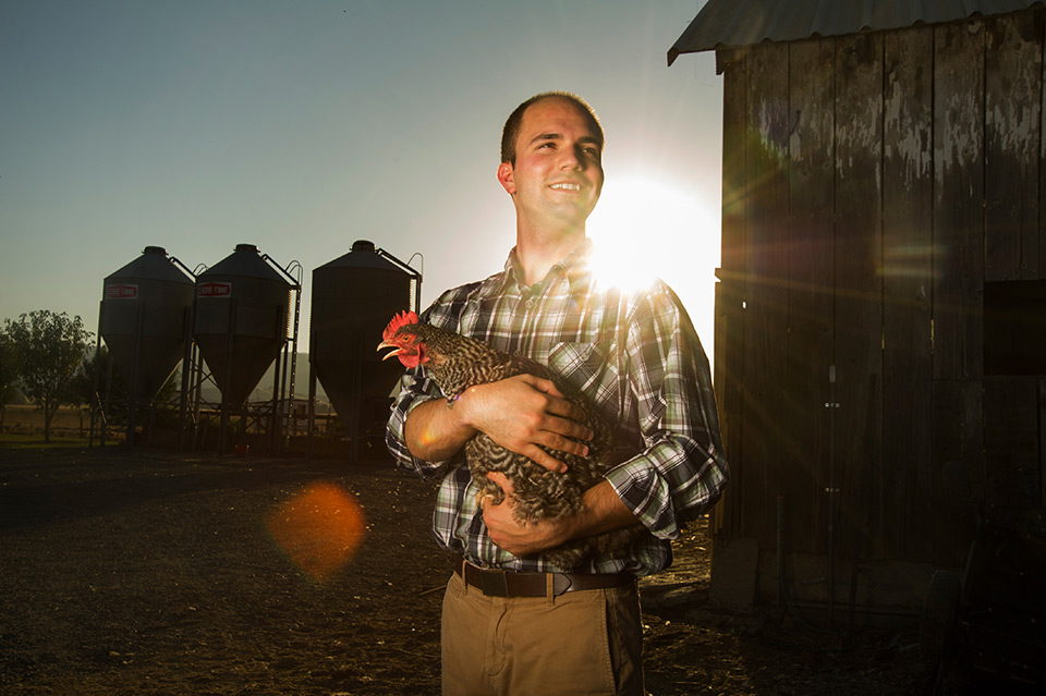  Award-winning photo of Edward Silva standing in front of a chicken coop while holding a hen.