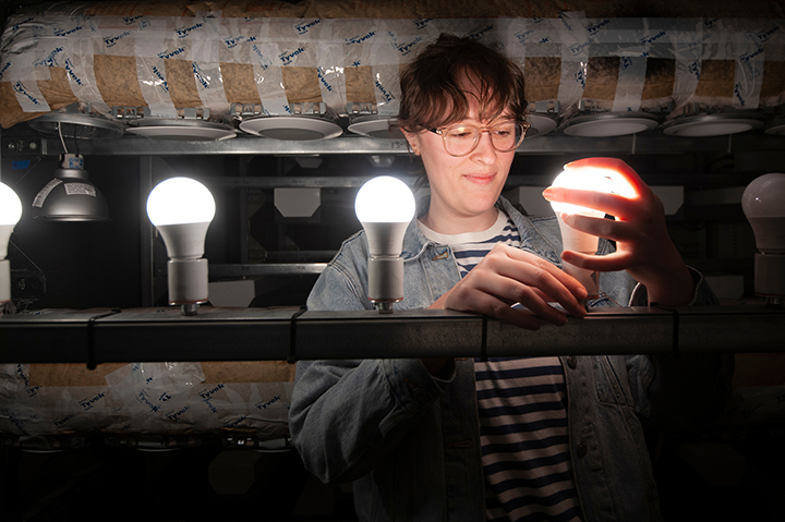 A student handles an illuminated lightbulb as they install LED lights in a testing room in a dark room.