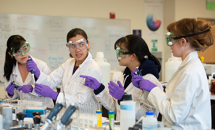 Four students wearing personal protective equipment work together in a science laboratory.