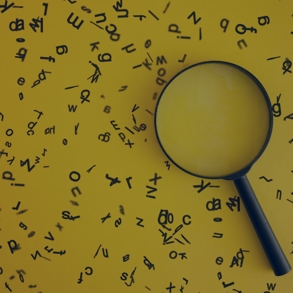 A bunch of letters scattered on a yellow field with a magnifying glass laying on top