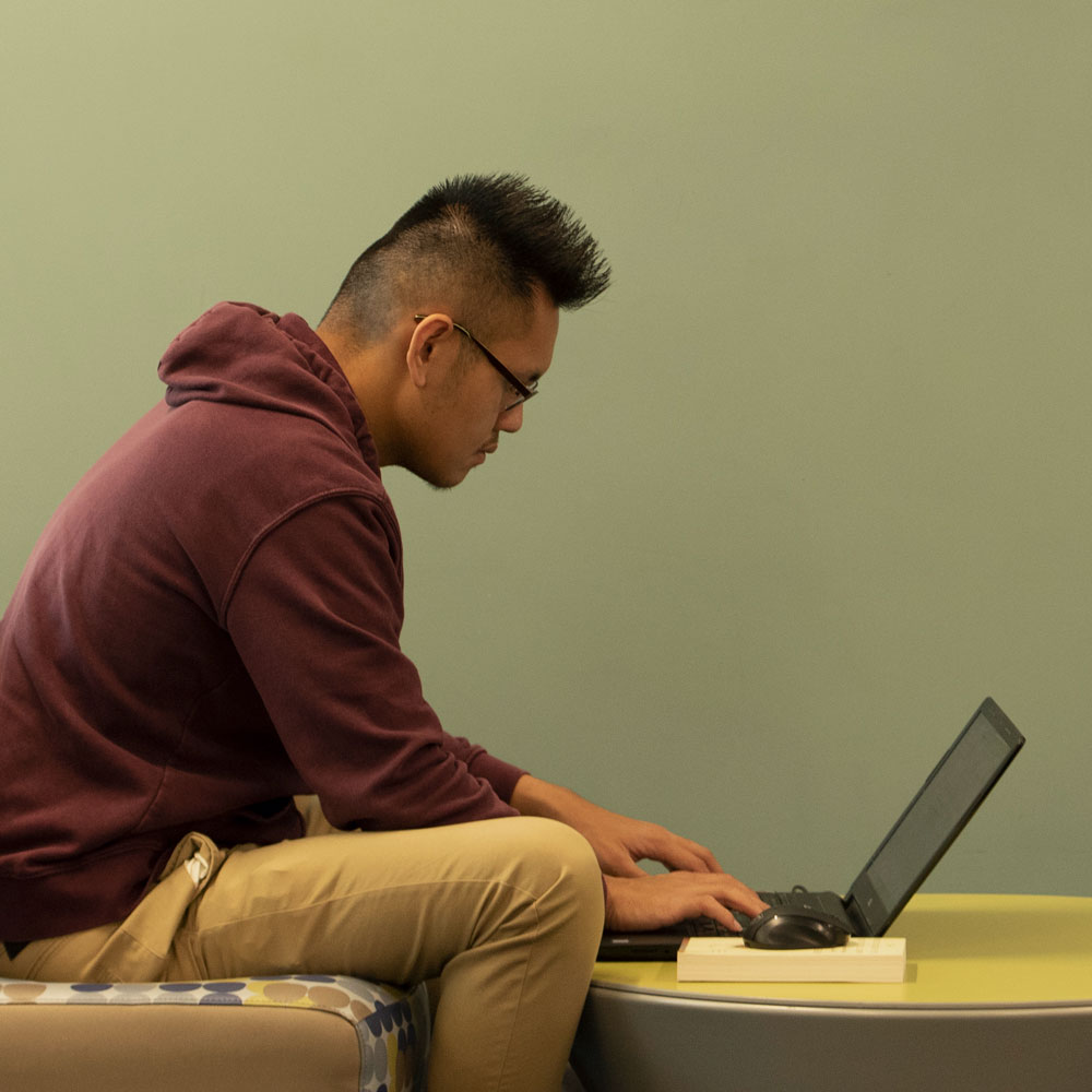 A student working on a laptop in front of a green wall