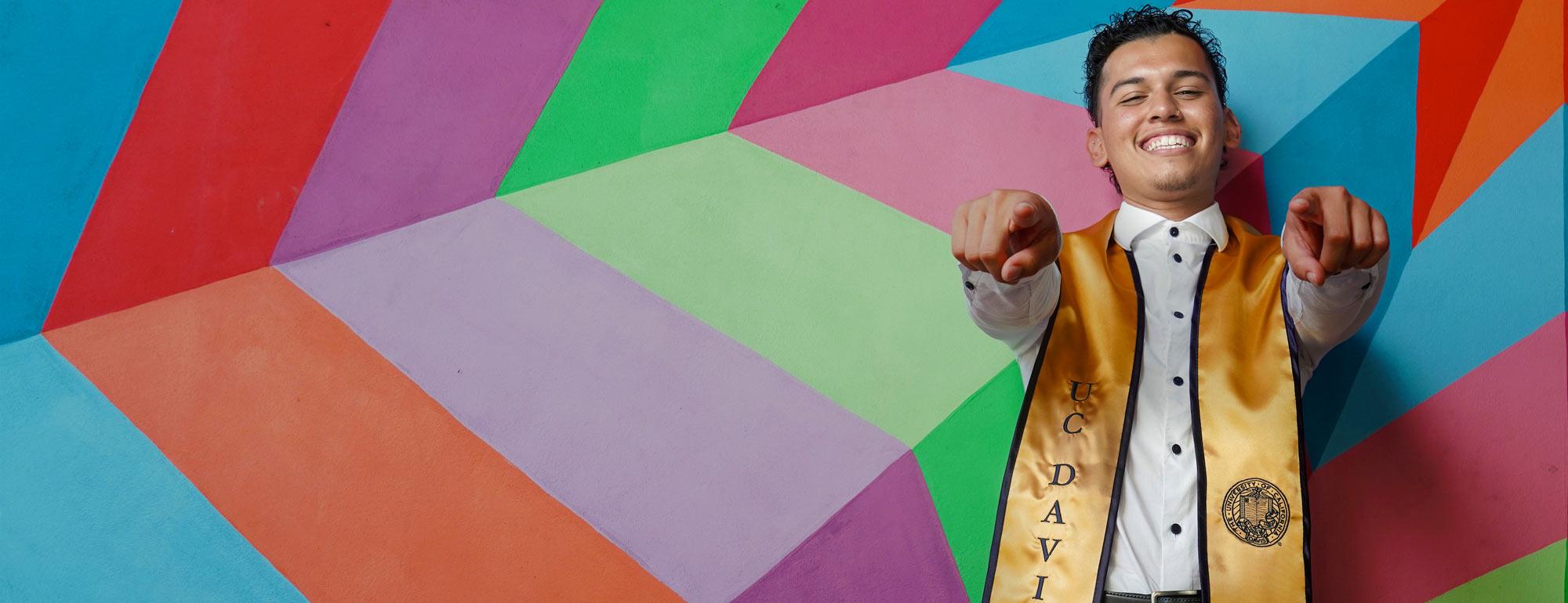A sdmiling student in front of a colorful wall