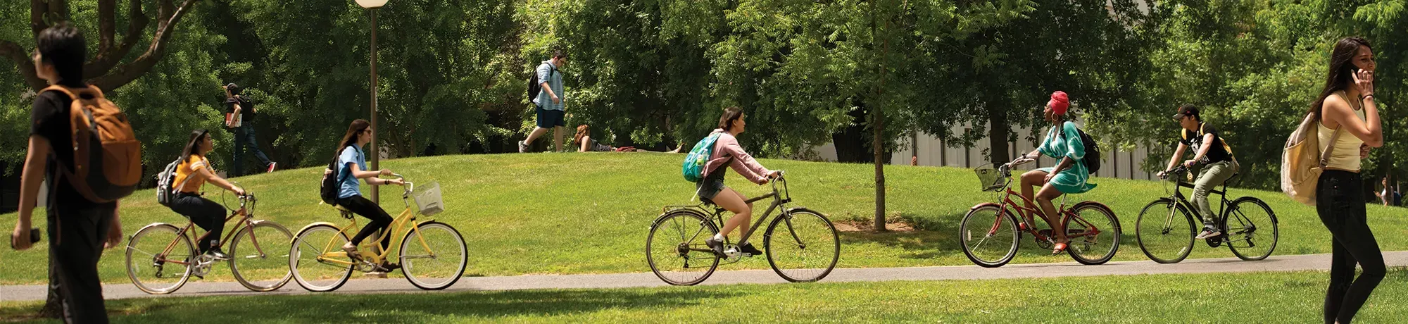 Composite photo of the UC Davis campus, with bikes and people riding and walking past the camera among small green hills and trees.